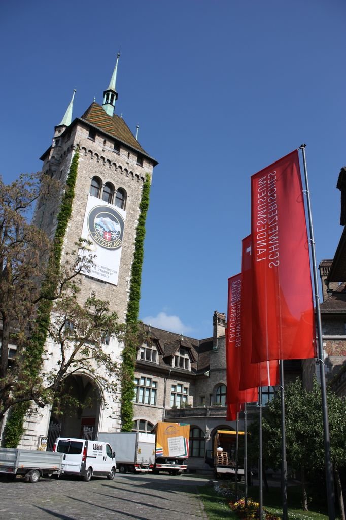 Historic museum entrance and tower in Zurich with red flags under clear blue skies.
